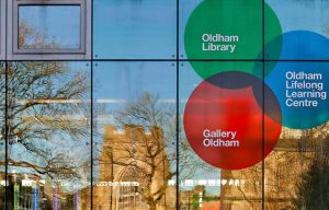 Oldham library window reflecting church and blue sky