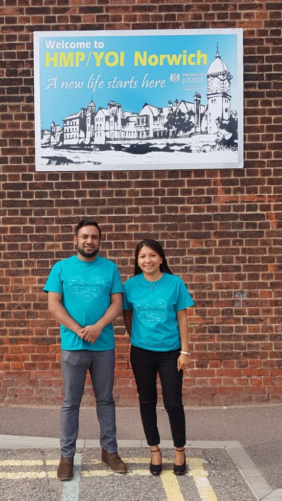 Gail and Koysar standing under a picture welcoming to HMP YOI Norwich a new life starts here