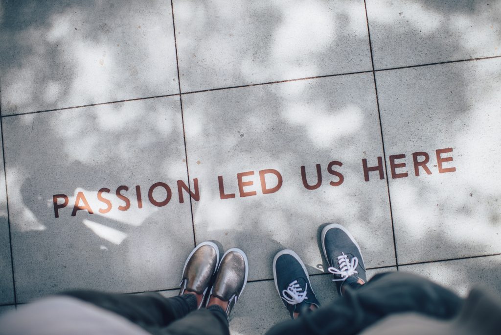 Two pairs of feet on a pavement with the caption "Passion led us here " written on the ground