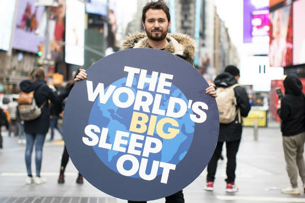 a man holding a large dark blue circular sign with a picture of the world on it and the words the worlds big sleep out in large white text