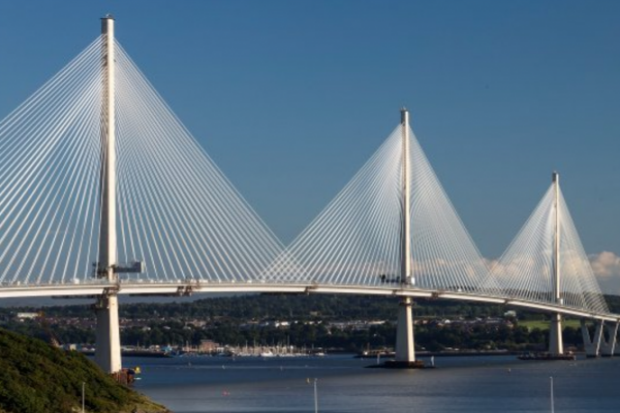 The Queensferry suspension bridge in the foreground across the Forth River with blue sky in the background.