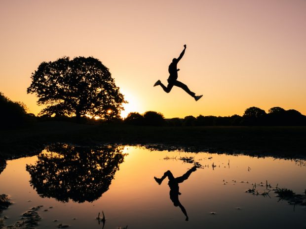 Man jumping over body of water during sunset