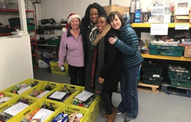 Four women standing by some crates of food in a warehouse at a foodbank