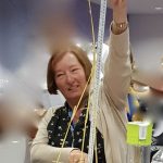 A woman is holding a tape measure to show the height of a tower made of spaghetti and marshmallows