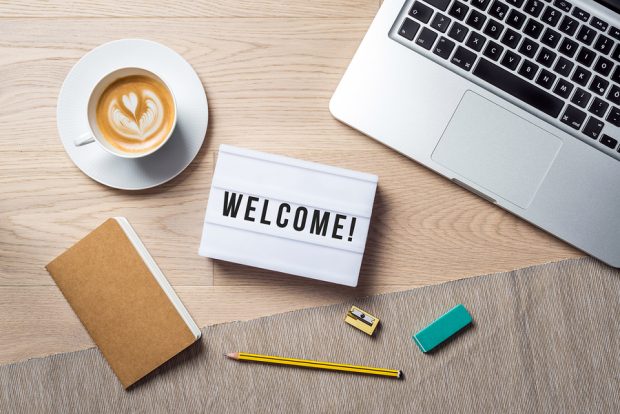 Welcome writing in lightbox lying on wooden desk with office supply and coffee cup as flat lay from bird's eye view