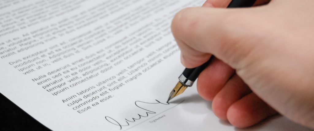 A hand holding a fountain pen signing an official looking document