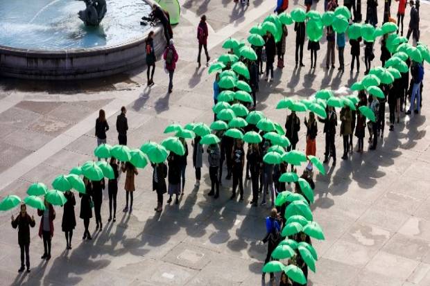 green ribbon of mental health depicted by people in the shape of the ribbon with green umbrellas covering their heads