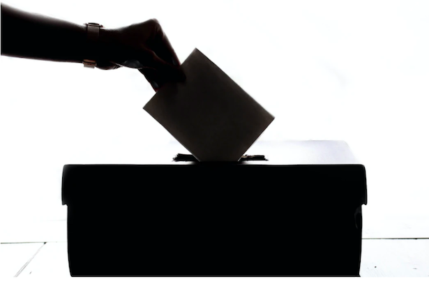 A ballot box in black and white with a hand posting a voting card through top
