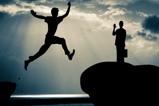 a silhouette of a person jumping over a gap to reach someone on the other bank