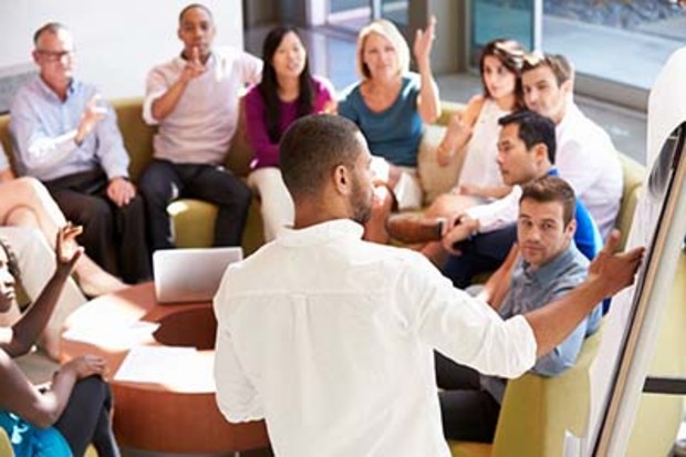 a group of people sitting around a flip chart being led by a facilitator