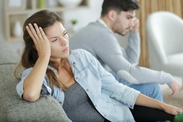 two people sitting on a sofa side on with their head in one hand