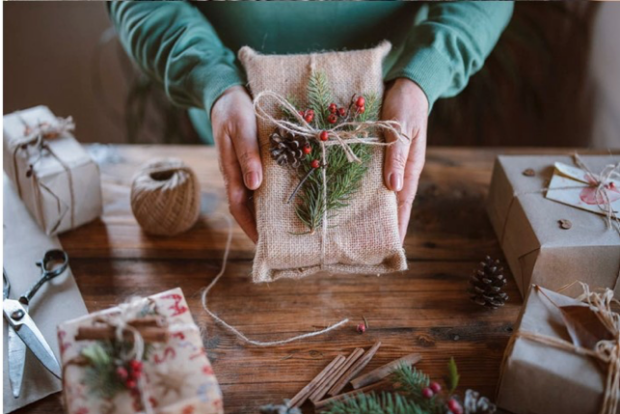 a pair of hands holding a present wrapped in hessiand with berries and conifer decorations